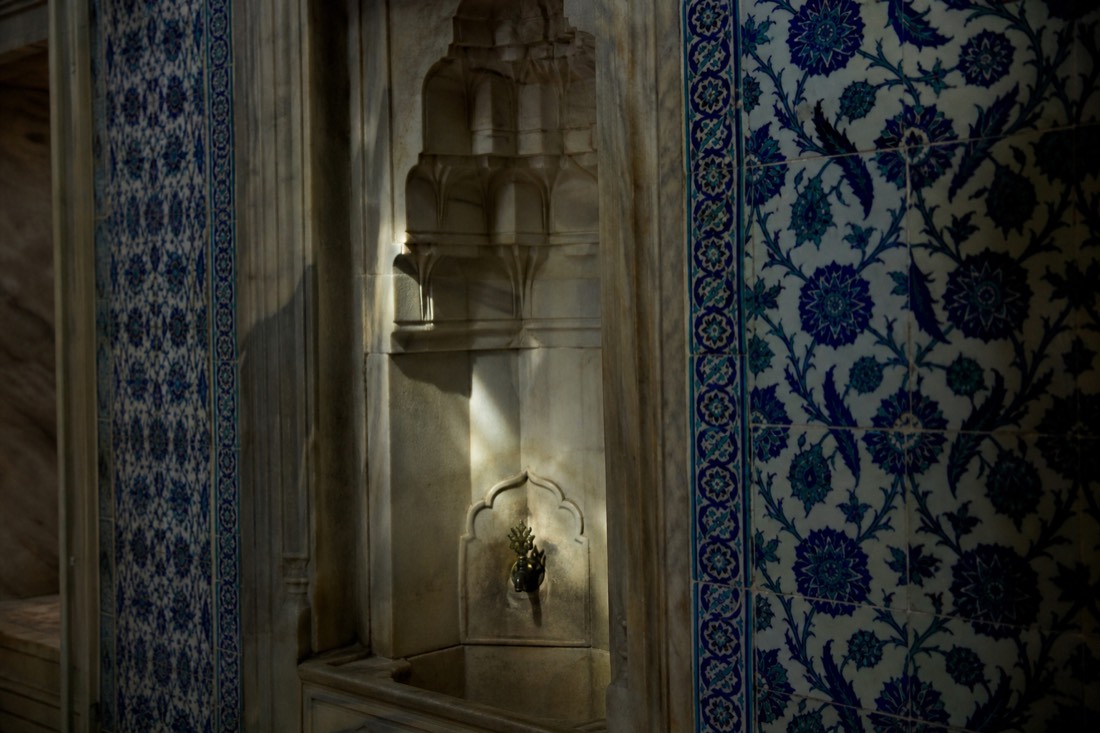 A marble wall fountain niche framed by Iznik tile panels in a dim Topkapi Palace interior