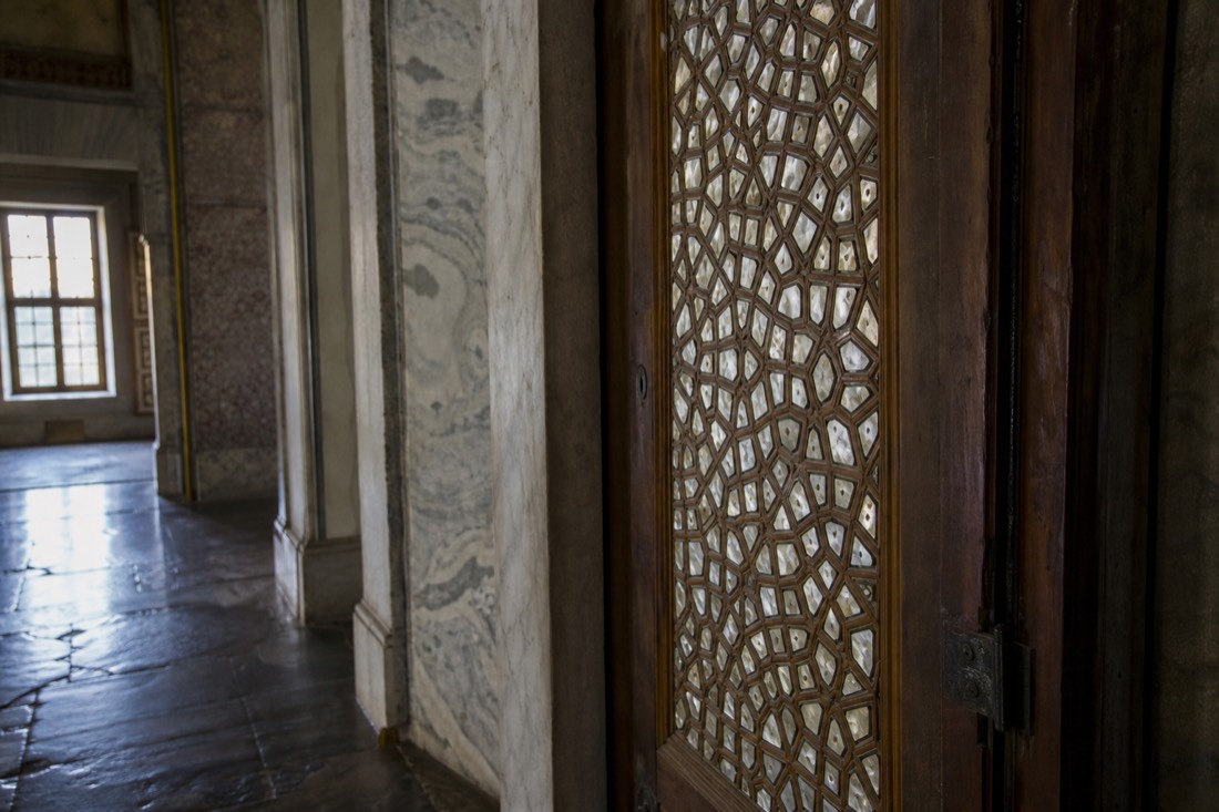 A marble Topkapi Palace doorway with mother-of-pearl inlaid doors seen at an angle in a dim interior