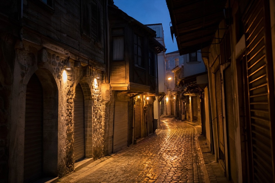 Narrow cobbled old-Istanbul lane near the Grand Bazaar with Ottoman-era shopfronts under evening lamplight